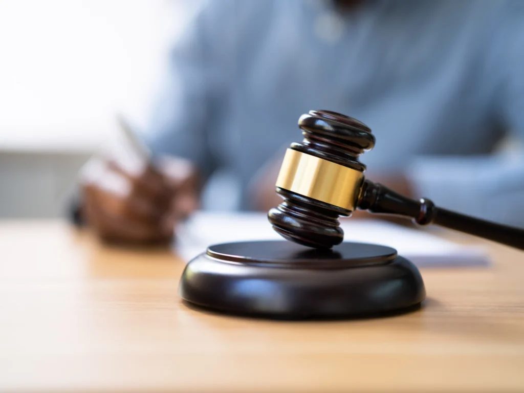 Richterhammer auf Tisch, unscharfe Person im Hintergrund schreibt