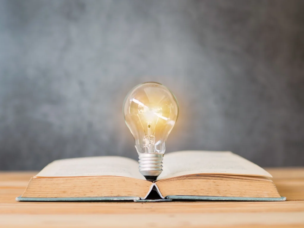 Glühbirne leuchtet auf offenem Buch – Symbol für Wissen und Ideen.