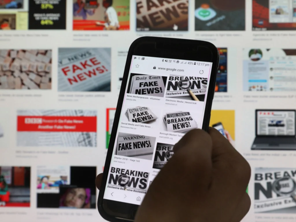 Smartphone mit „Fake News“-Suchergebnissen vor Bildschirm