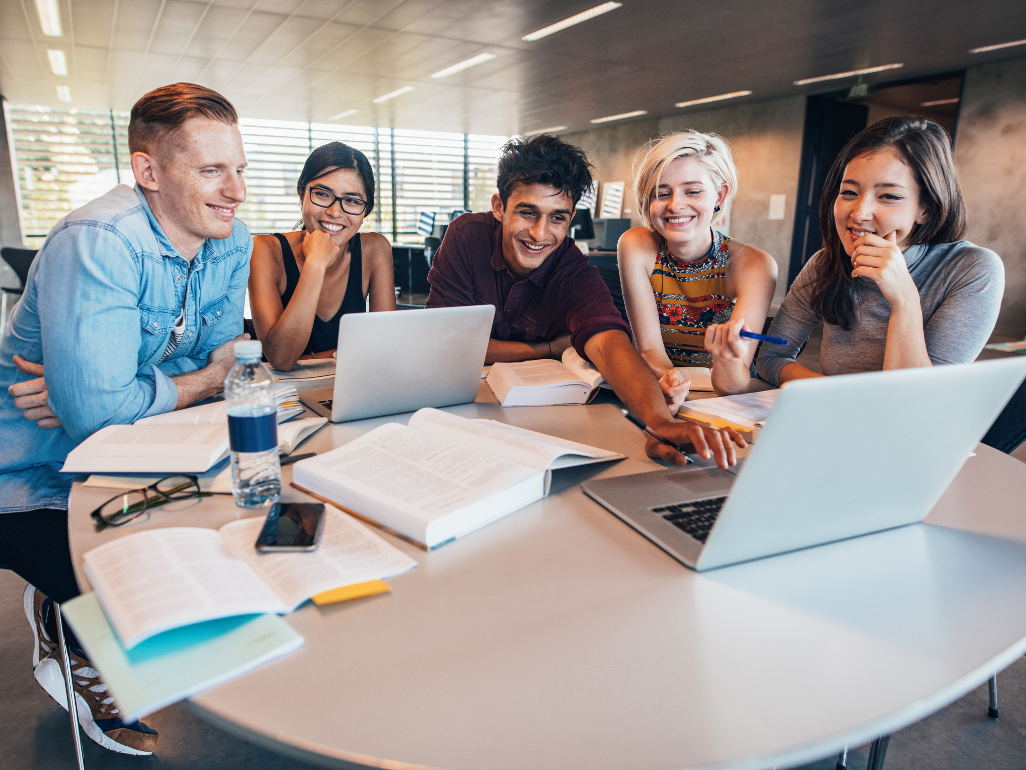 Studierende arbeiten gemeinsam am Tisch mit Laptops und Büchern